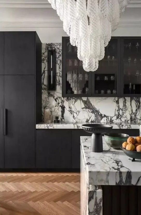 a sophisticated black and white kitchen with matte black cabinets and white marble countertops and a backsplash plus a stunning crystal chandelier