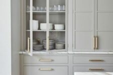 a sophisticated dove grey kitchen with flat panel and glass front cabinets and white marble countertops plus gold handles