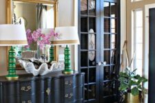 a sophisticated entryway with a striped rug, a black dresser, black French doors, a large mirror, antlers and table lamps