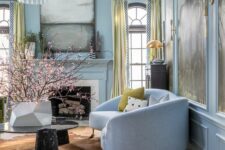 a sophisticated pastel blue living room with a non-working fireplace, a chic curved sofa, yellow curtains and pillows and a statement chandelier