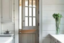 a stained wood Dutch door adds a rustic feel to the all-white kitchen with paneling and makes it more welcoming