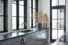 a stylish and elegant grey kitchen with shaker cbainets, black countertops, black framed windows and a door