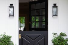 a stylish black and white farmhouse entrance with a black Dutch door, potted greenery, black wall sconces and layered rugs