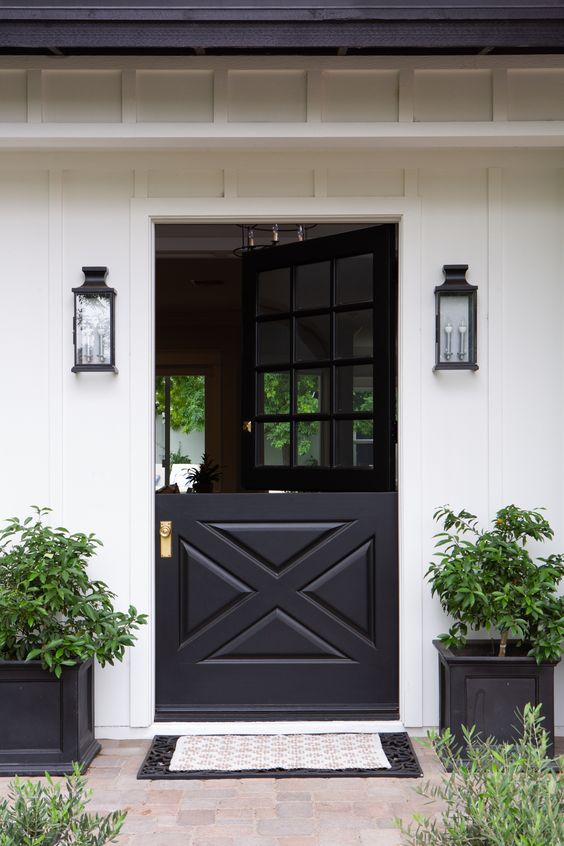 a stylish black and white farmhouse entrance with a black Dutch door, potted greenery, black wall sconces and layered rugs