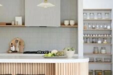 a stylish grey kitchen clad with skinny tile, with an open shelf instead of upper cabinets, an open pantry, a fluted curved kitchen island with a white stone countertop