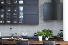 a stylish kitchen with black cabinets, a wooden kitchen island, black leather stools and a black hood