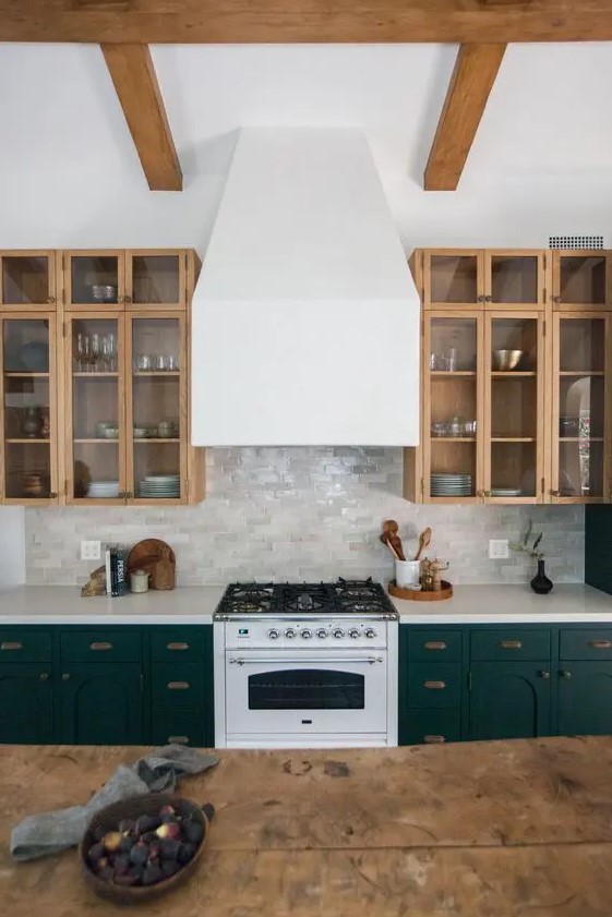 a stylish kitchen with dark green and stained kitchen cabinets, arches and glass ones, with a glossy tile backsplash and a white hood