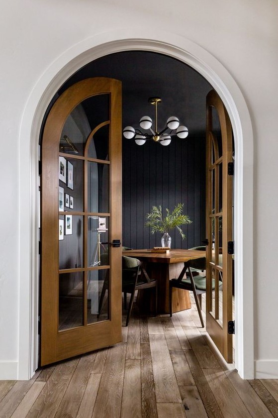 a stylish moody dining room with a stained table and green chairs and stained arched wood frame doors that highlight the style