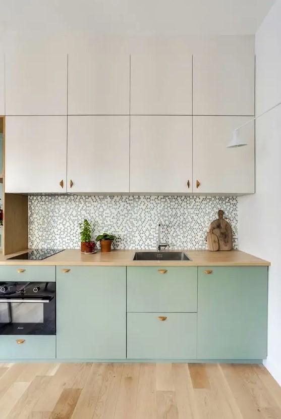 a two-tone kitchen with creamy and mint green cabinets, a printed tile backsplash, butcherblock countertops and built-in appliances