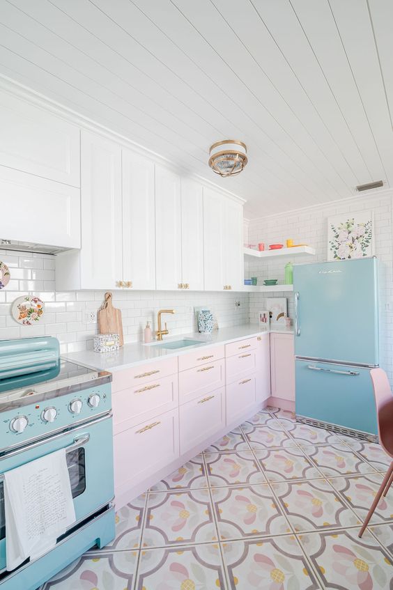 a two-tone kitchen with white and pale pink shaker cabients, a blue fridge and a cooker plus a printed tile floor