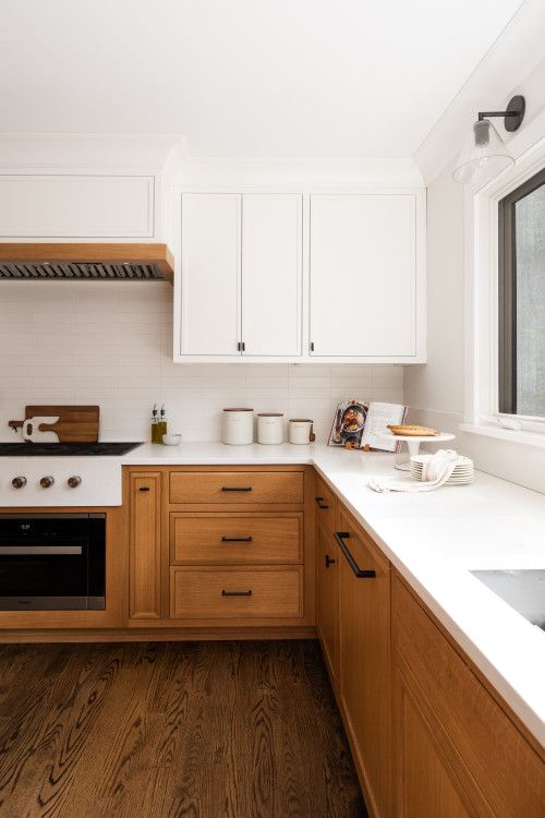 a two-tone kitchen with white and stained cabinets, black panels, white countertops and white skinny tiles is chic