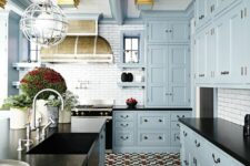 a vintage dusty blue kitchen with shaker cabinets, black granite countertops, a colorful tile floor and a cage pendant lamp