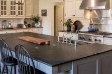 a vintage farmhouse kitchen with creamy shaker cabinets, wooden beams and a blue grey kitchen island with a black countertop