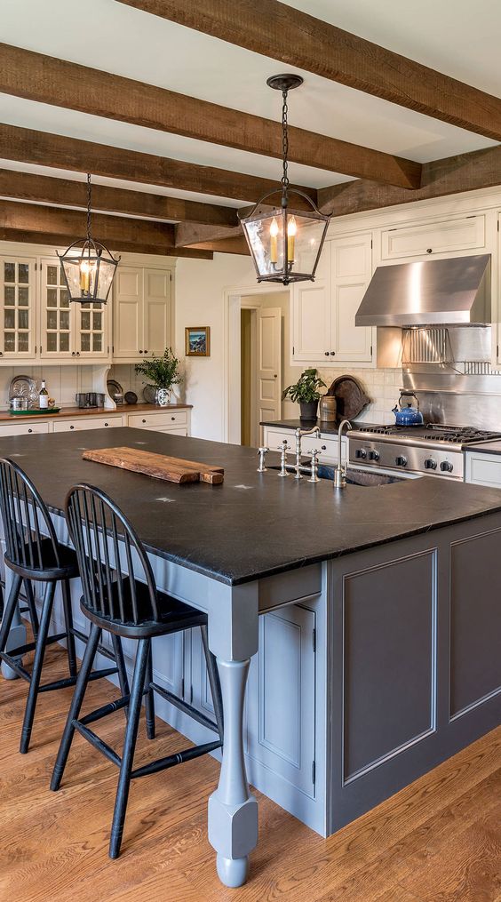 a vintage farmhouse kitchen with creamy shaker cabinets, wooden beams and a blue grey kitchen island with a black countertop