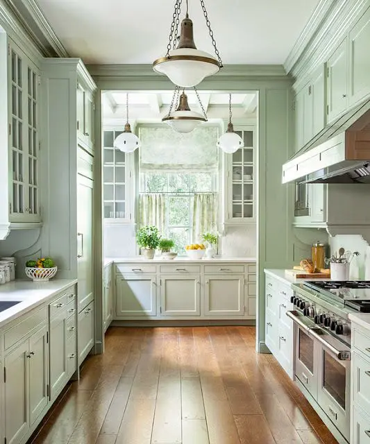 a vintage mint green kitchen with shaker cabients and glass front ones, white stone countertops, vintage chandeliers and lots of windows