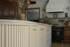 a vintage stained kitchen with shaker cabinets and a creamy fluted and curved kitchen island, brass pendant lamps