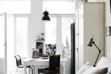 a white Scandinavian meets shabby chic bedroom with a bed and a wardrobe, a white desk and dark chairs, some art and black lamps