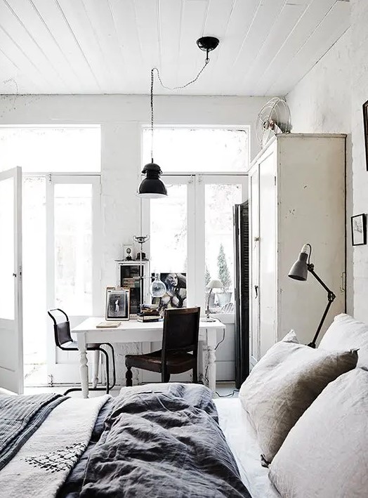 a white Scandinavian meets shabby chic bedroom with a bed and a wardrobe, a white desk and dark chairs, some art and black lamps