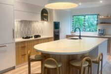 a white and stained kitchen with a skinny til backsplash, a curved kitchen island, tall stools, pendant lamps and lights