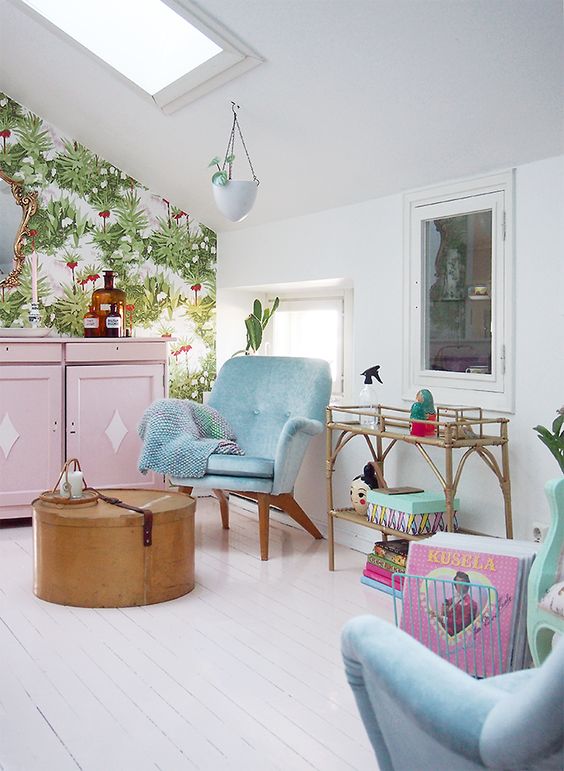 a white attic living room with pastel blue chairs and a pink cabinet, a rattan table and a round box, a botanical wallpaper accent wall