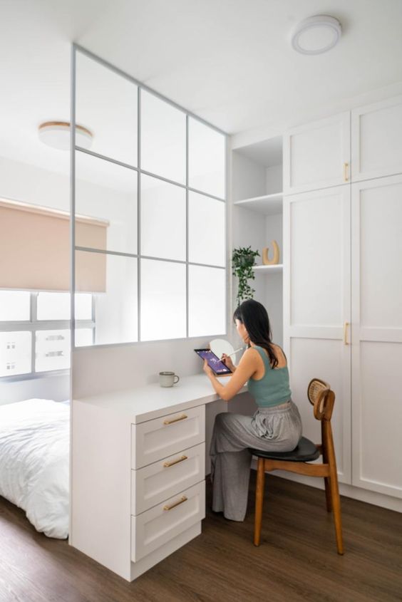 a white bedroom slit in two parts, a sleeping zone by the window, a space divider and a desk, a wardrobe
