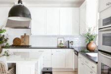 a white farmhouse kitchen with shaker cabinets, black countertops, a large white kitchen island, a black pendant lamp
