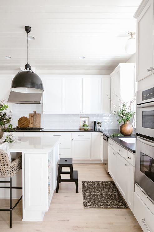 a white farmhouse kitchen with shaker cabinets, black countertops, a large white kitchen island, a black pendant lamp