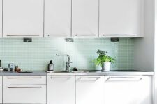 a white mid-century modern kitchen with a mint tile backsplash and grey countertops, stainless steel fixtures