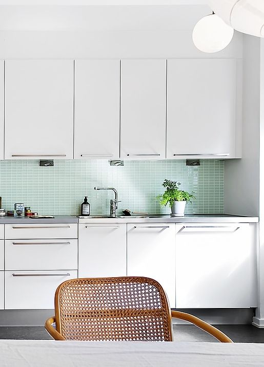 a white mid-century modern kitchen with a mint tile backsplash and grey countertops, stainless steel fixtures