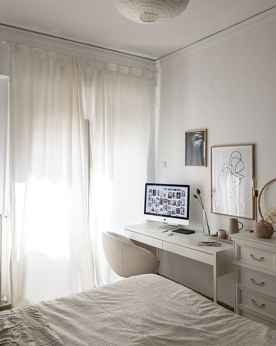 a white bedroom with a bed, a small IKEA desk, a neutral chair, an elegant dresser, artwork and neutral textiles