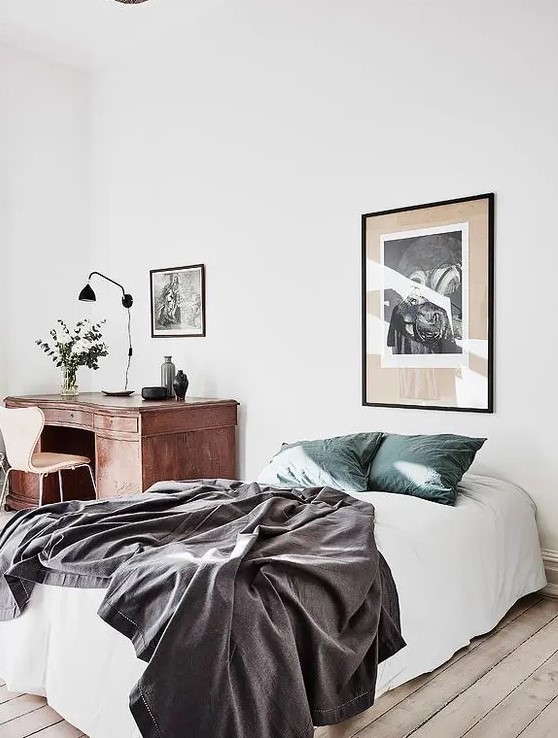 an airy and light bedroom with a bed and a vintage wooden desk in the corner, some artwork to make it more beautiful and stylish