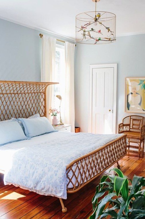 an airy blue bedroom with light blue walls, a rattan bed and chairs, light blue bedding and a bold artwork