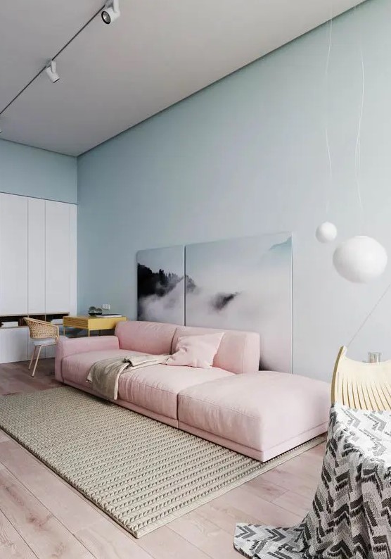 an airy pastel living room with pastel blue walls, a pink low sofa, a statement artwork, a white storage unit, a woven rug