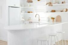 an all-white kitchen with sleek plain cabinets, a curved ribbed kitchen island that is an accent here, open shelving instead of upper cabinets