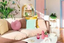 an awesome pastel living room with a blush sofa, pastel pillows, a pink floral artwork, a bright rug, a pink door and a tiered table