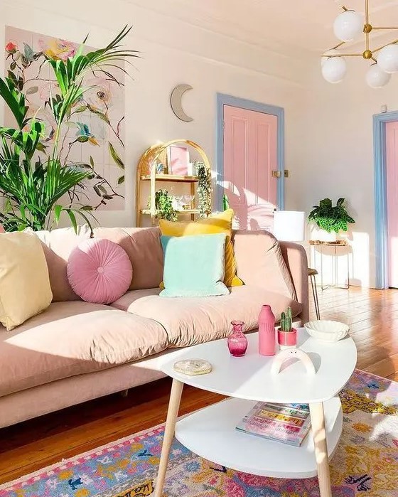 an awesome pastel living room with a blush sofa, pastel pillows, a pink floral artwork, a bright rug, a pink door and a tiered table