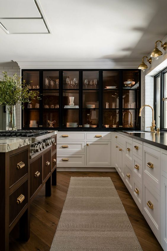 an elegant and refined kitchen with white lower cabinets, large black frame and smoked glass cabinets and a dark-stained kitchen island