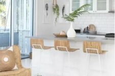 an inspiring beach kitchen with white cabinets, a kitchen island, woven pendant lamps, wooden sotols, a wicker chair and a matching tray