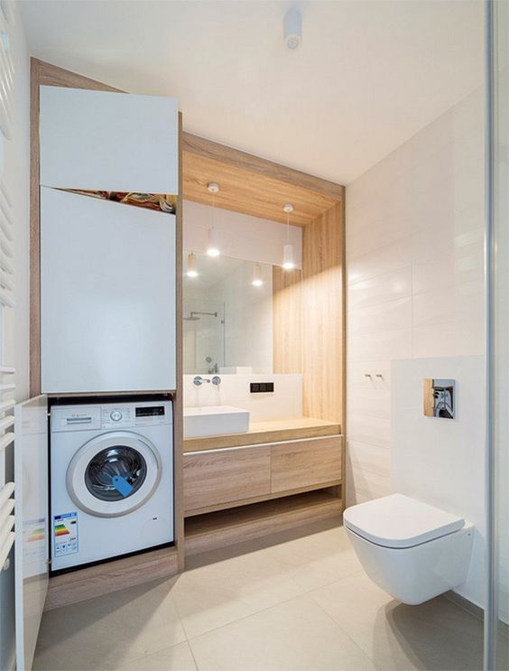 a minimalist neutral bathroom clad with large scale tiles, with a washing machine built in, a built-in vanity and a toilet