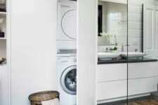 09 a modern white bathroom clad with large scale tiles, a white vanity with a black countertop, a large white storage unit with a washing machine and a dryer