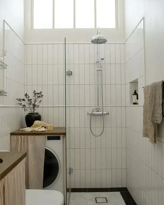 a tiny black and white bathroom with skinny white tiles and black and white ones, a small shower space, a washing machine with a curtain