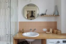 21 a mid-century modern bathroom with a bathtub, an open timber vanity with a washing machine, dusty pink tiles and a round mirror