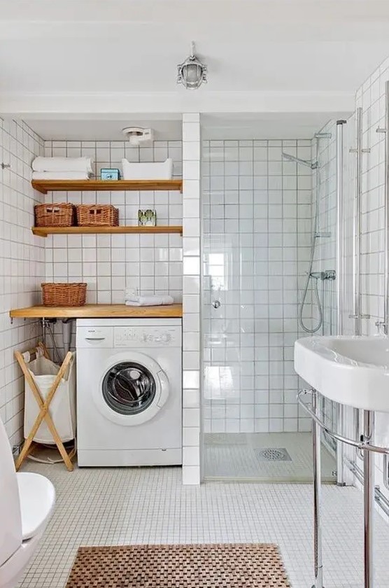 a modern white bathroom clad with square tiles, with a laundry nook with shelves and a washing machine,a shower space and a sink