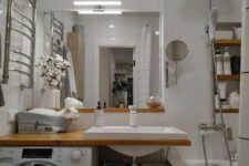 26 a modern white bathroom with a bathtub, an open timber vanity with a washing machine, a mirror and built-in shelves