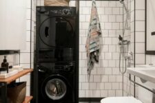 29 a Scandinavian bathroom with white square and black hex tiles, a wooden shelving unit, a shower and stacked washing machine and a dryer