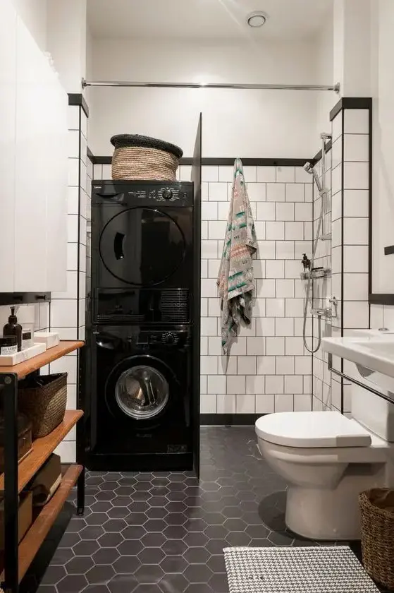 a Scandinavian bathroom with white square and black hex tiles, a wooden shelving unit, a shower and stacked washing machine and a dryer