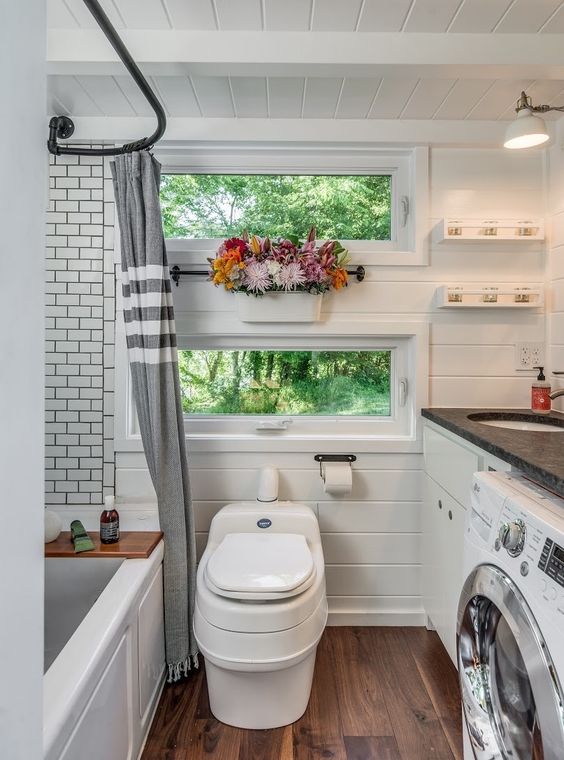 a small and cozy bathroom clad with beadboard and subway tiles, a tub, a washing machine and some shelves