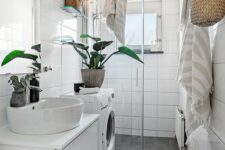 33 a small bathroom clad with large scale tiles, with a shower space, a washing machine and a white vanity, potted plants and baskets