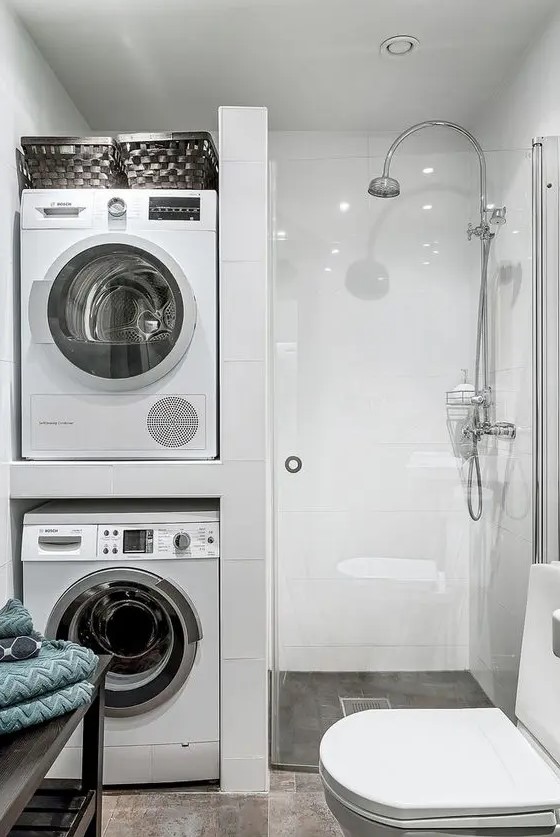 a small minimal bathroom with a washing machine and a dryer, a shower space, a white toilet and a black shelving unit