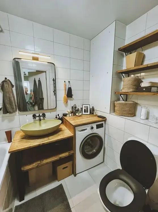 a small white bathroom clad with white tiles, with wooden shelves and an open timber vanity plus a built in washing machine